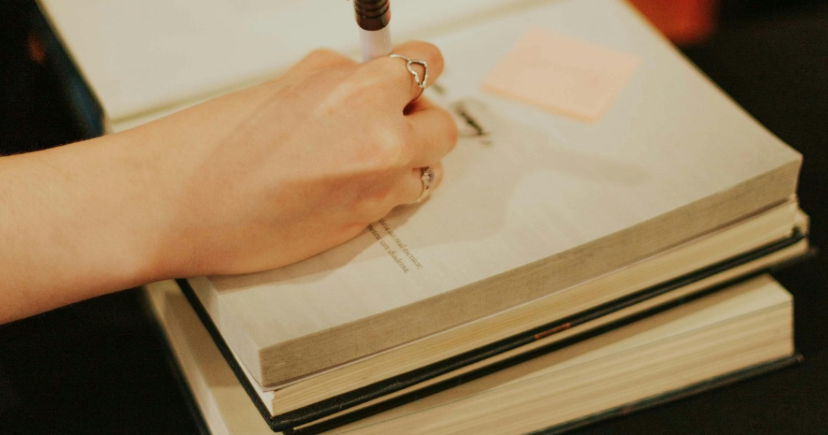 Imagen de la mano de una mujer escribiendo en un libro.