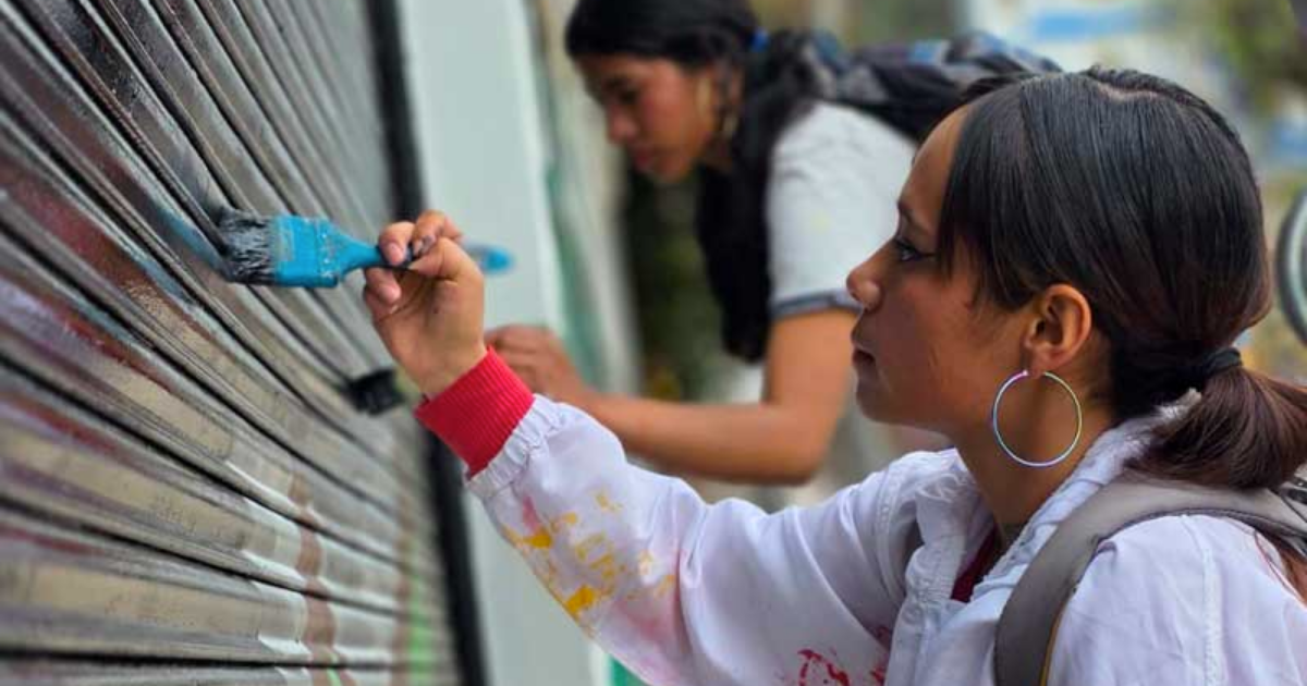 Imagen de dos mujeres jóvenes que pintan la fachada de una casa.