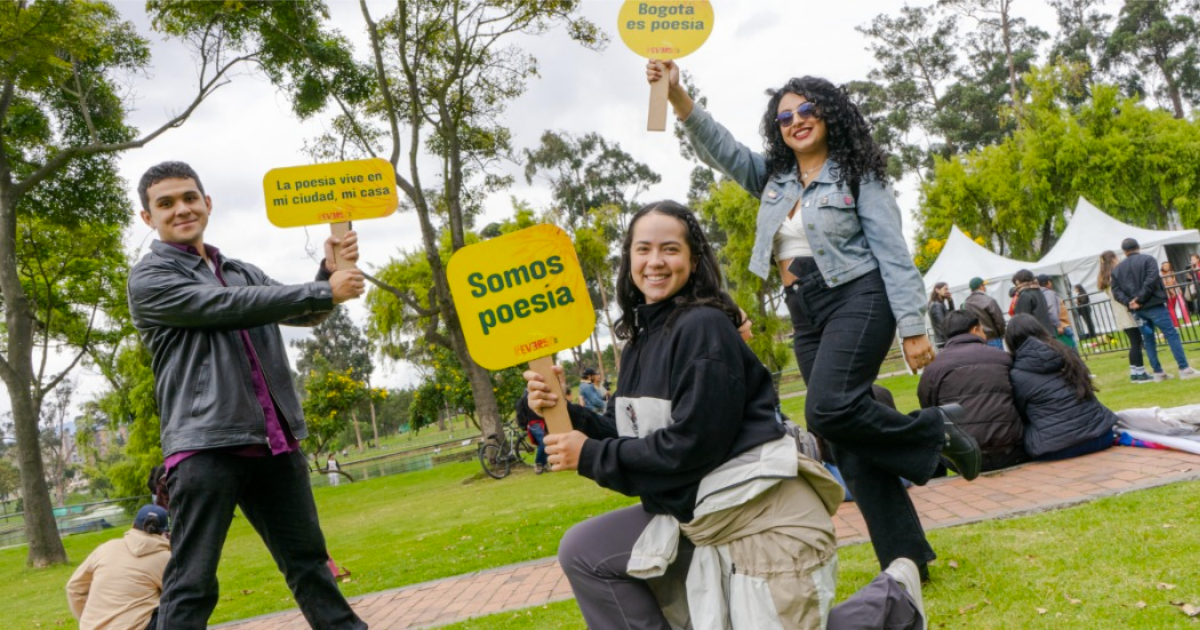 Imagen de dos mujeres jóvenes y un hombre que se encuentran en un parque, en sus manos llevan carteles con info del Festival Reverso.