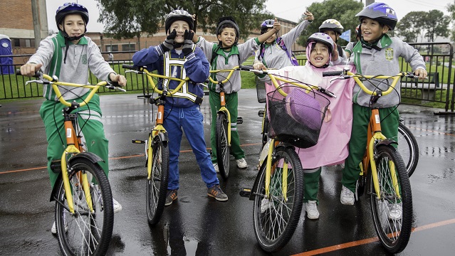 Varios niños montados en sus bicicletas sonriendo y saludando a la cámara 