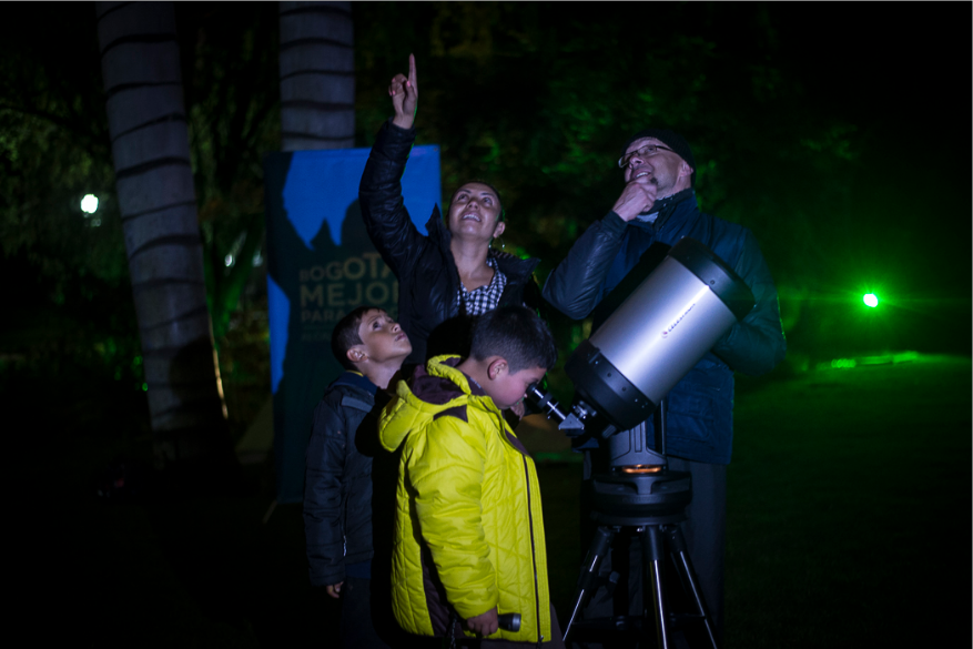 Varios adultos y niños observando el cielo por un telescopio 