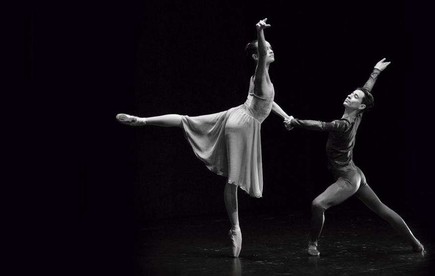 Un hombre y una mujer bailarines de ballet, cogidos de la mano realizando una pose de su danza