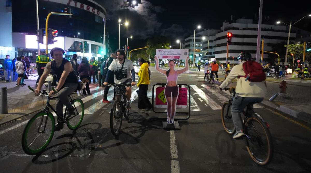ciclistas recorren calle de Bogotá en jornada de Ciclovía Nocturna con publicidad de sensibilización de espacios seguros para las mujeres