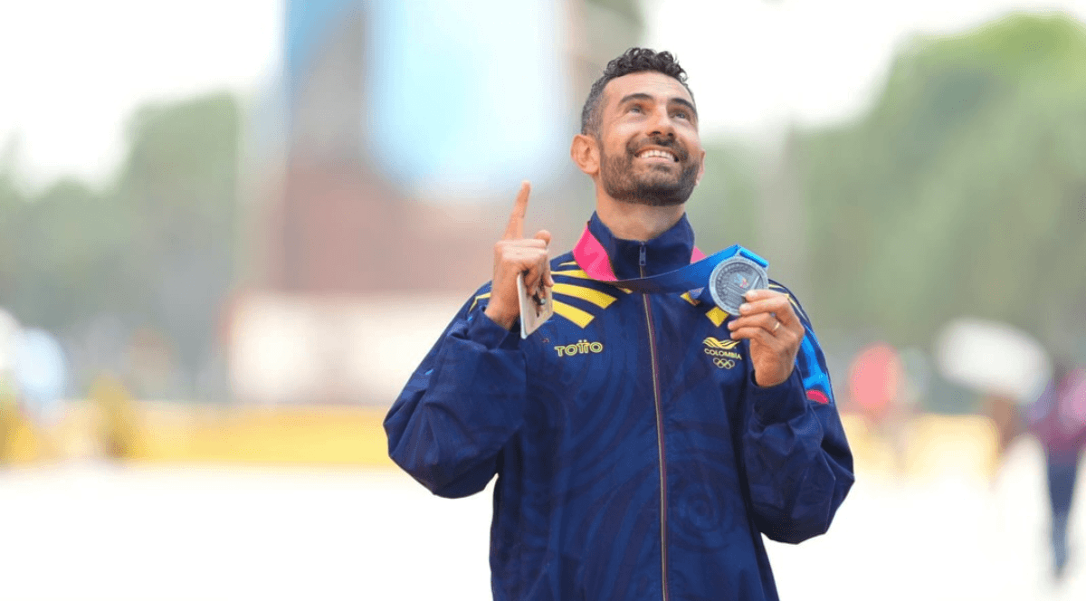 Eider Arévalo con chaqueta de la delegación olímpica de Colombia sostiene una medalla colgada al cuello mientras señala hacia arriba con una mano en Juegos Olímpicos París 2024.