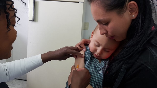 Una enfermera aplicando una inyección a un bebe que abraza a su mama