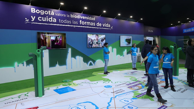 El stand de la Alcaldía de Bogotá en la Feria Internacional del Libro de Bogotá, varios funcionarios con la chaqueta azul caminan alrededor del stand 