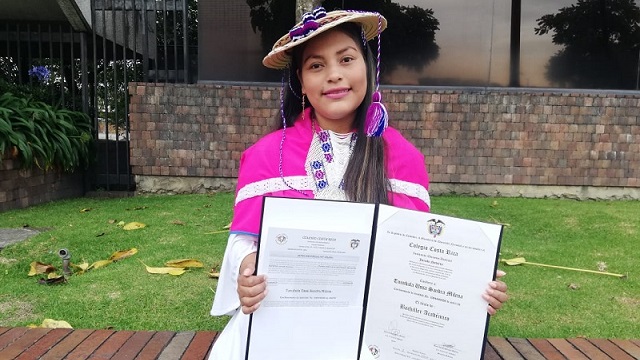 Una mujer de la comunidad sosteniendo su diploma de graduación frente a la camara 