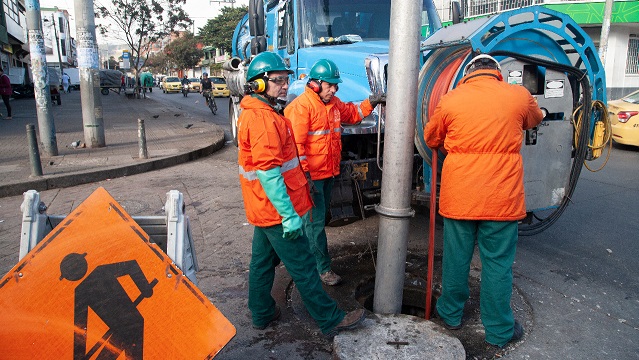 Tres hombres del Acueducto de Bogotá trabajan con maquinaria en un hueco de la calle 