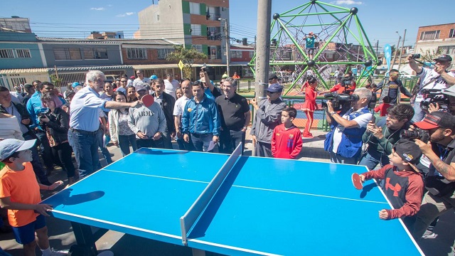 El Alcalde Enrique Peñalosa jugando tennis de mesa con un niño en el nuevo parque de Engativá, rodeado de personas de la comunidad 