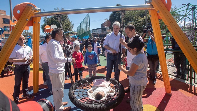 El Alcalde Enrique Peñalosa jugando en un columpio alrededor de las personas de la comunidad