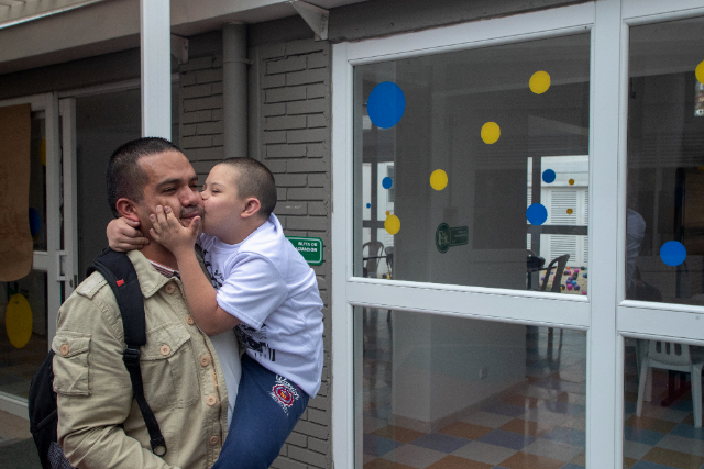 Un hombre tiene en brazo a un niño, y el niño le esta dando besos en el cachete 