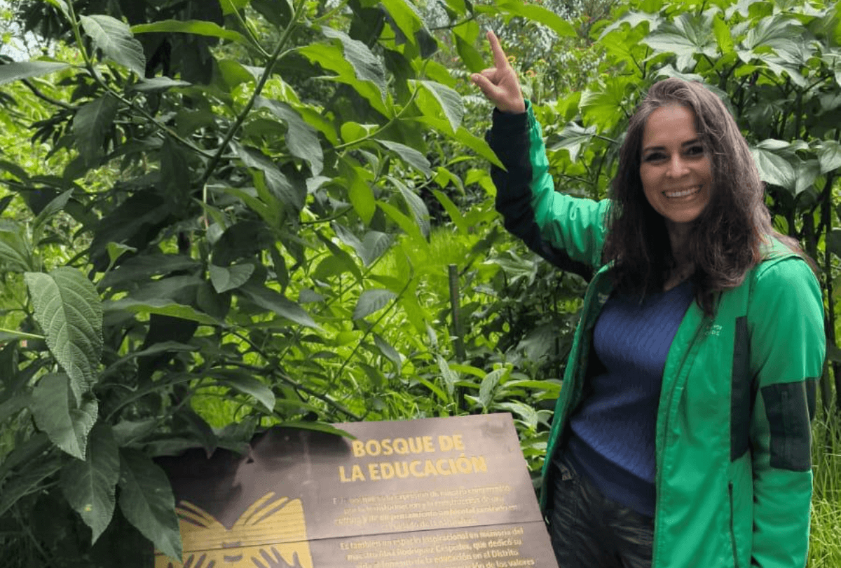 Tania Rodríguez señala el letrero con texto literal “Bosque de la Educación” durante recorrido entre vegetación nativa y procesos de restauración ecológica del Jardín Botánico de Bogotá.