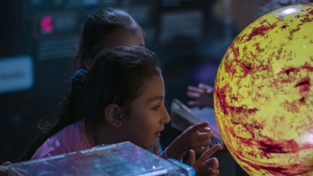 Primer plano de una niña observando una maqueta del sol a escala pequeña