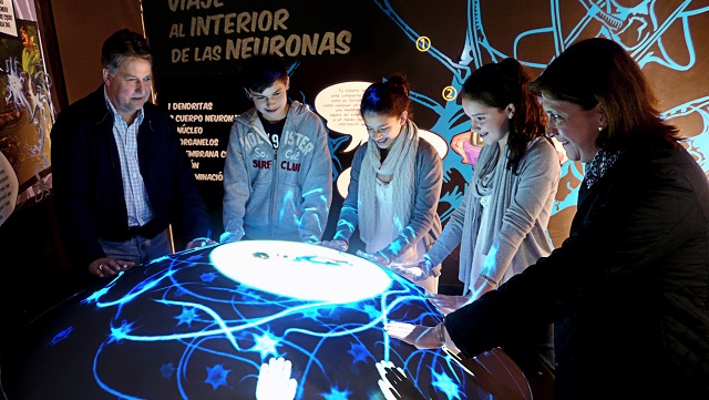 Cinco personas alrededor de un aparato redondo que emite luz azul y les enseña las diferentes constelaciones
