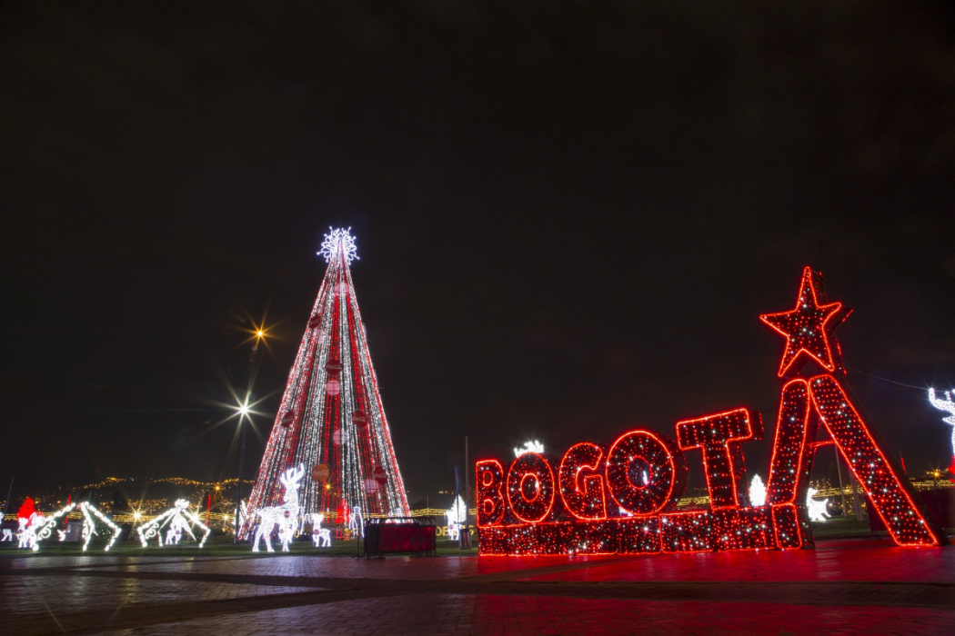 La noche en uno de los parques de la ciudad, al fondo el árbol de navidad y el logo de Bogotá encendido en luces de color rojo.