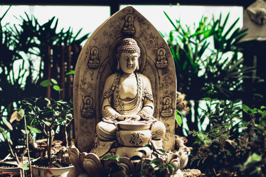 Una estatua mediana de un buda meditando en un pequeño jardín.