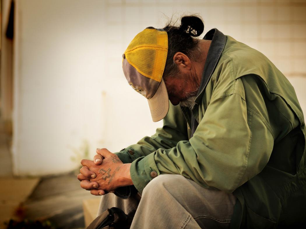 perfil de un hombre de avazada edad en situación de tristeza y pobreza sentado con cabeza abajo y manos cruzadas