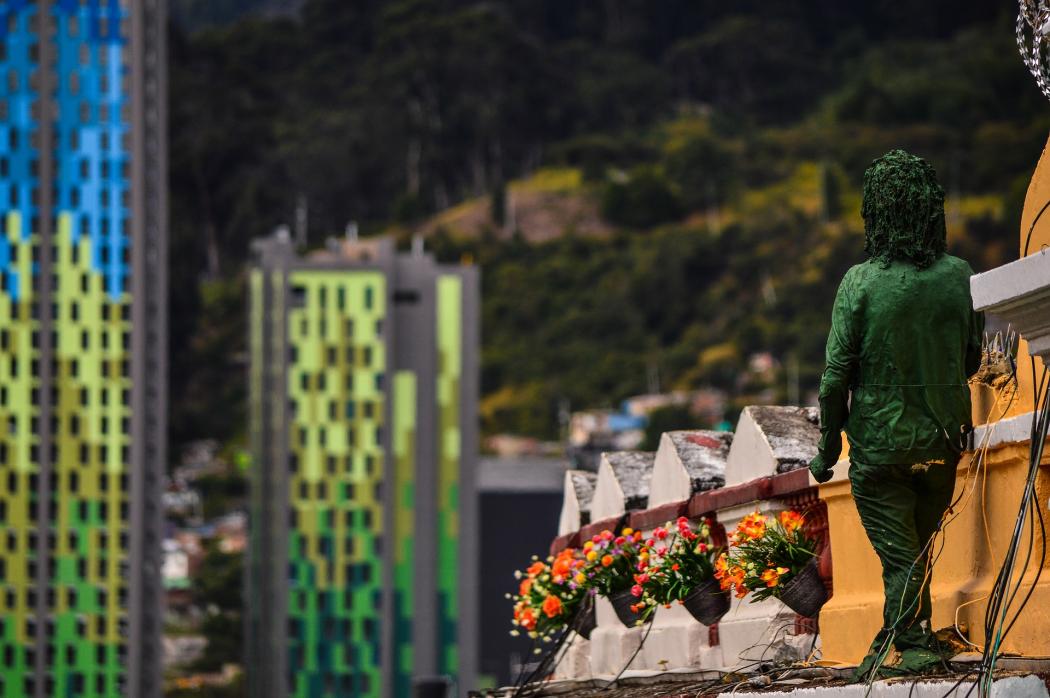 Foto de la escultura verde de un niño, al fondo hay varios edificios de colores 