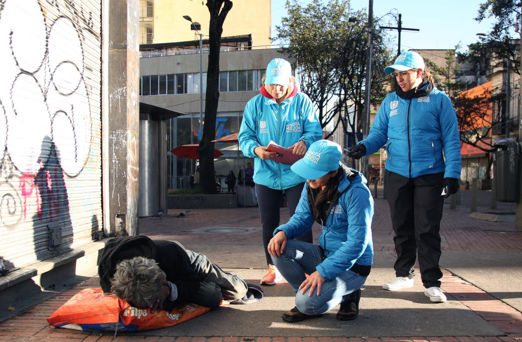 Tres trabajadores de la Secretaría Social acompañan a un habitante de calle que esta acostado en la calle