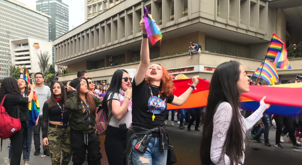 Mujer blanca de cabello rojizo sostiene una bandera de la comunidad LGBTI en la marcha por sus derechos en Bogotá.