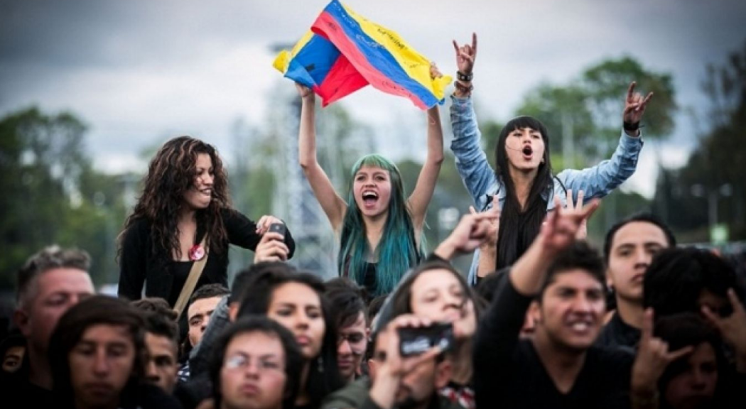 Un grupo de jóvenes rockeros disfrutan de Rock al Parque mientras sostienen una bandera de Colombia.