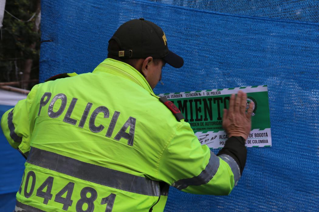 Un policía de espaldas colocando un sello de cerrado a un establecimiento comercial 