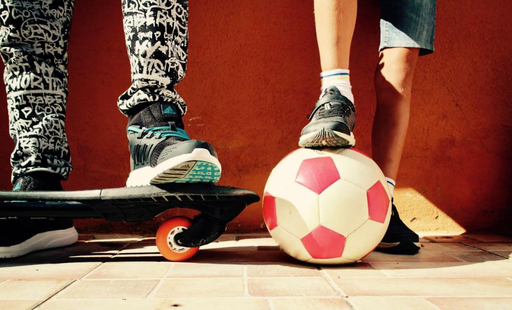 Imagen de los pies de jóvenes con un balón de fútbol y una patineta 