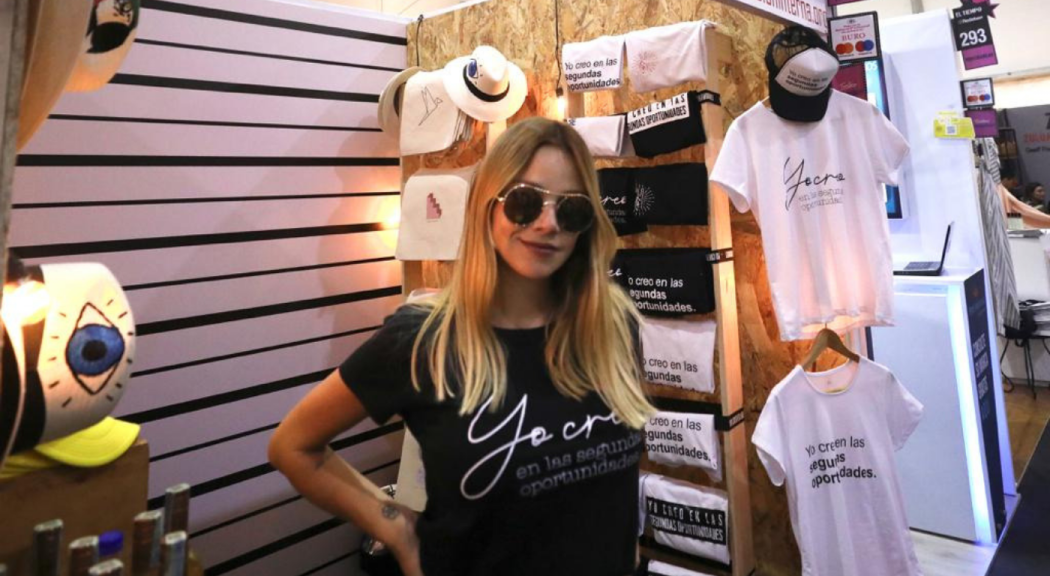 Actriz y activista Johana Bahamón posa en el stand de Buró con camisetas y sombreros fabricados por personas privadas de la libertad. 