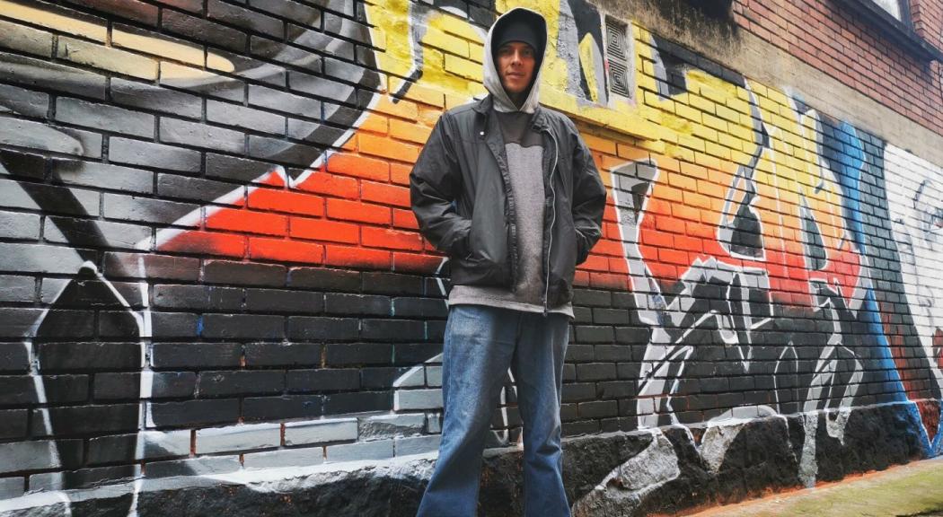 Ricardo Acosta posa frente a una pared pintada con un graffiti.
