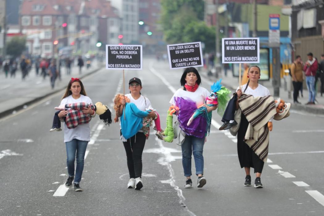 Mujeres marchan con muñecos de trapo entre sus brazos, representan a líderes sociales asesinados.