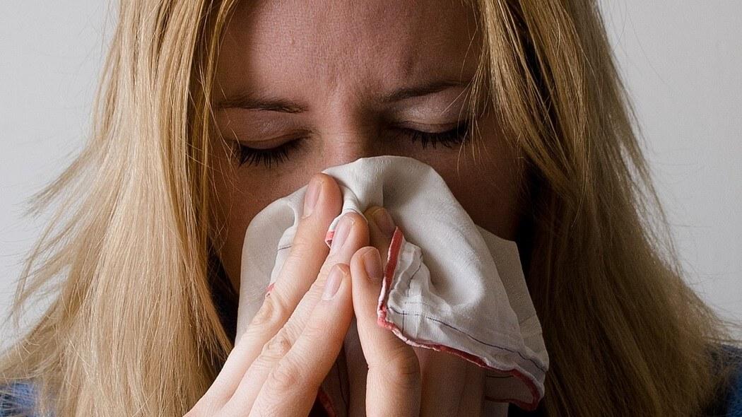 Imagen de una mujer estornudando y tapándose con un pañuelo 