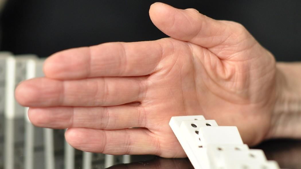 fotografía de una mano deteniendo la caída de un dominó