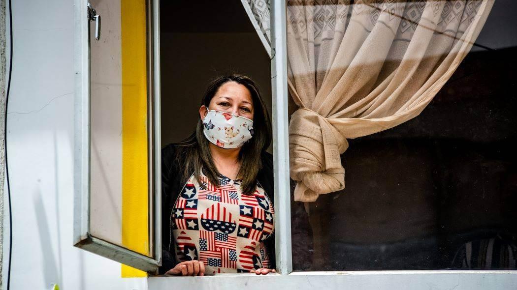 Imagen de una mujer mirando desde su ventana con tapabocas puesto