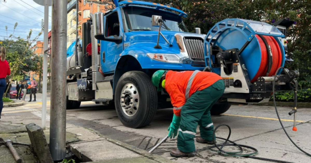 Imagen de trabajador del Acueducto de Bogotá realizando trabajos en la tubería de una calle, ubicado frente a un carro de la empresa