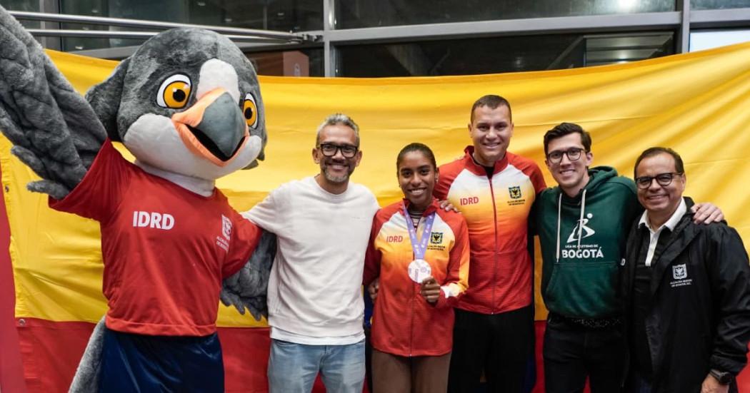 Deportista de Bogotá recibiendo reconocimiento por parte de directivos y mascota oficial 