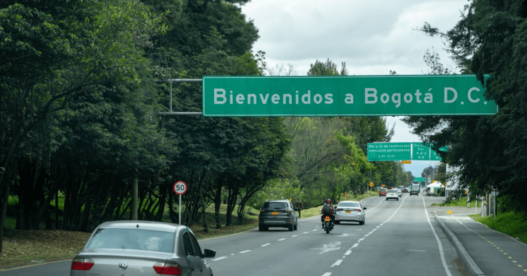 Foto de la entrada a Bogotá por una vía rodeada de árboles y un cartel que da la bienvenida