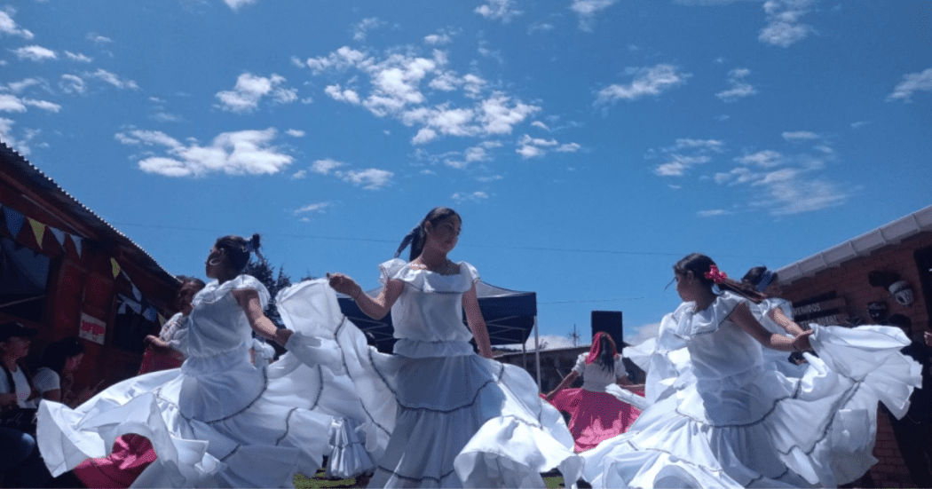 Imagen de mujeres bailando cumbia con vestidos típicos blancos y de fondo se ve un bello cielo azul