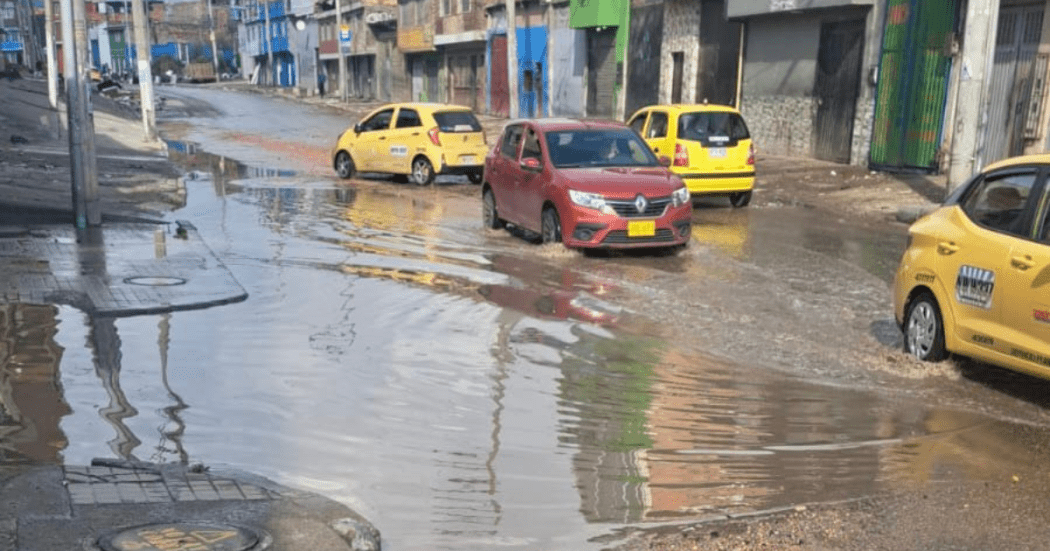 Foto de unos carros al lado de un charco de agua en Bogotá 