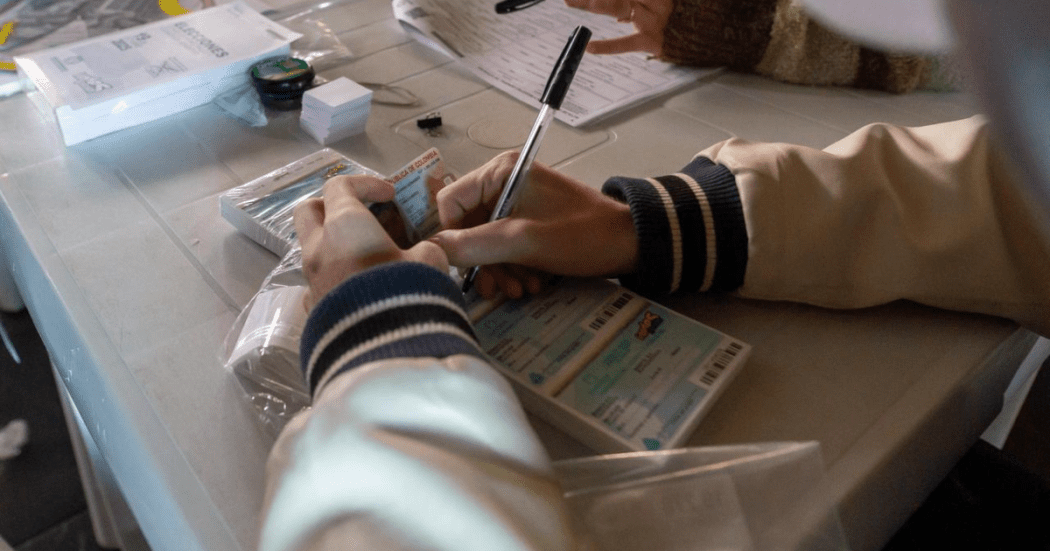 Imagen de las manos sosteniendo un esfero sobre una papeleta de votación