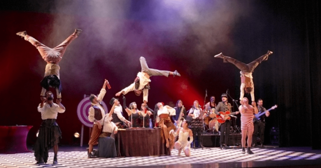 Imagen de una puesta en escena de lo que parece ser una obra de circo, de fondo el escenario se pierde por las luces y neblina.