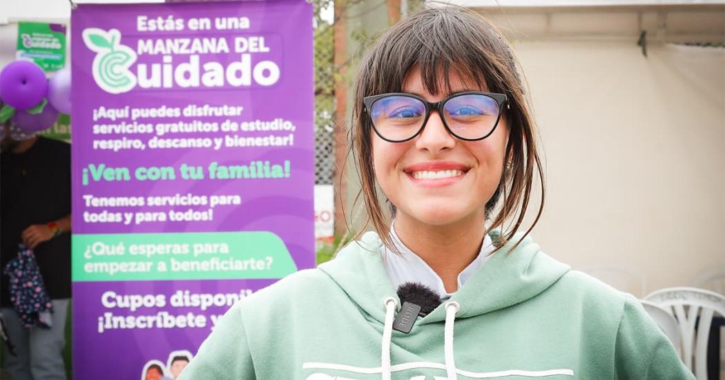 En la foto una mujer sonriendo y atrás un cartel con los servicios de la secretaría de la mujer