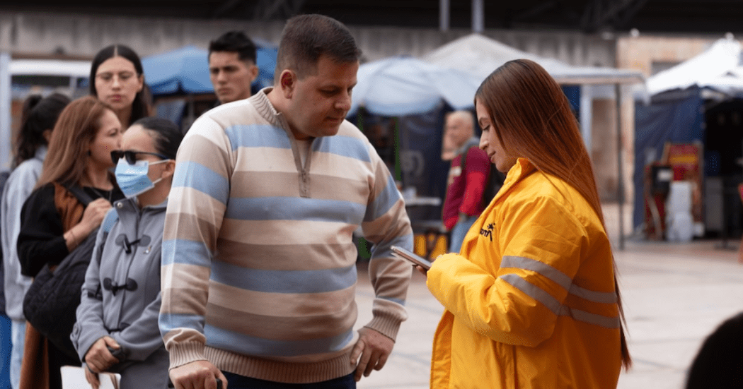 Imagen de una funcionaria pública atendiendo a un hombre en una fila