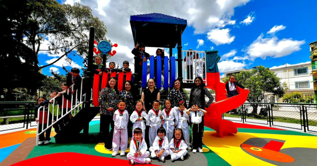 Foto de un grupo de niños y adultos disfruta un colorido parque infantil recién renovado bajo un cielo despejado