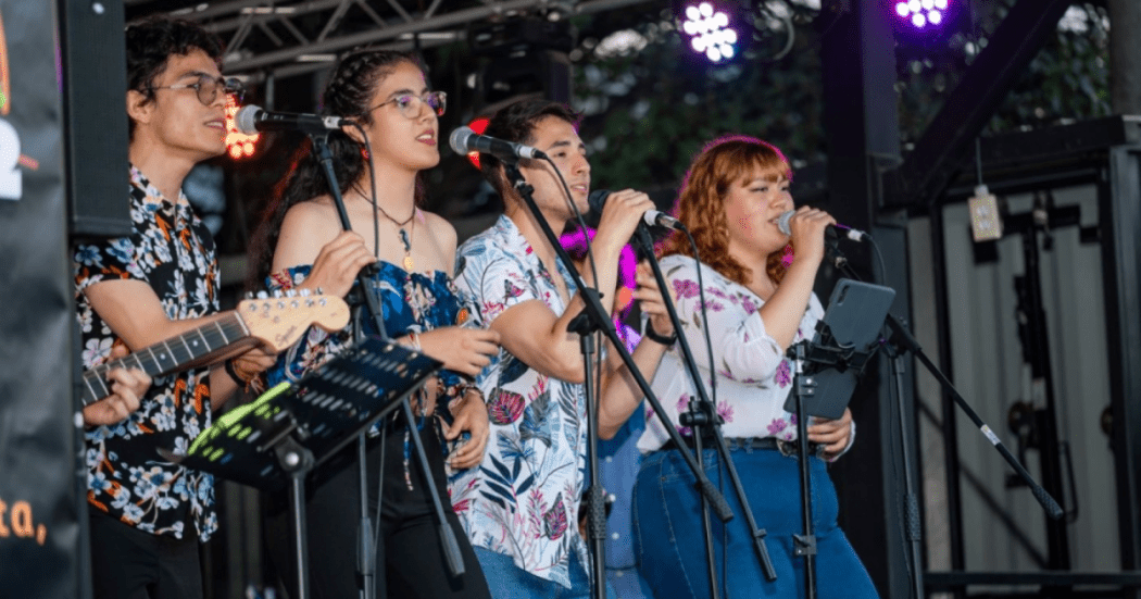 Foto de un grupo de jóvenes músicos interpretando en vivo sobre un escenario al aire libre.