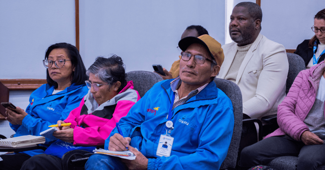 Foto de personas que escuchan atentamente y toman notas durante un espacio de diálogo ciudadano.