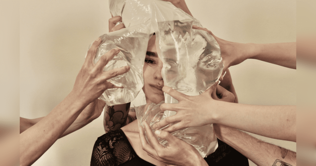 Imagen de la cara de una mujer, a su alrededor hay muchas manos de personas que tienen bolsas plasticas llenas de agua que al presionar su cara se ve desfigurada.
