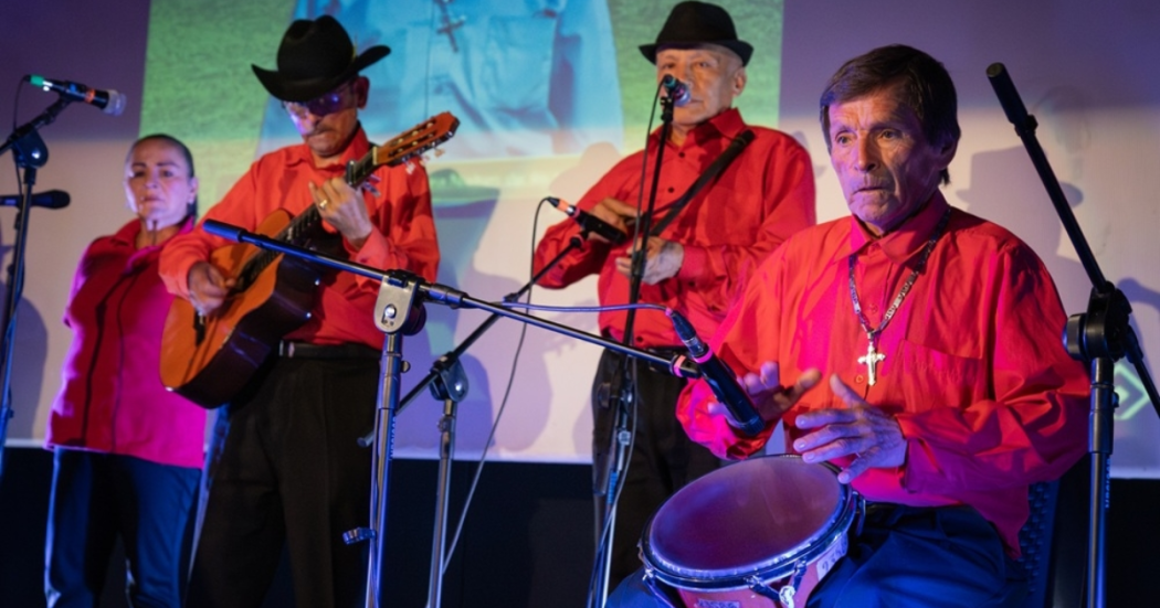 Imagean de unos músicos de orquesta vestidos con camisa roja y sombrero negro, que tocan sus instrumentos
