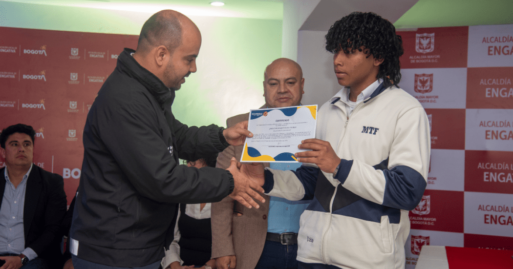 Imagen de un estudiante recibiendo un diploma simbólico de la beca