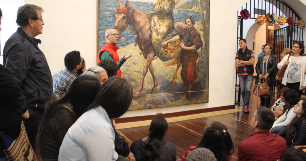 Imagen de varias personas en sala de un museo escuchando atentamente al guía.