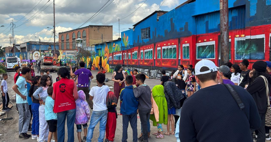 Foto de un grupo de niños y vecinos observando un mural colorido del Tren de la Sabana durante una actividad comunitaria en Los Mártires.